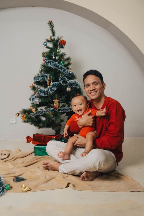 Free Father and baby celebrate Christmas indoors with a decorated tree and gifts. Stock Photo