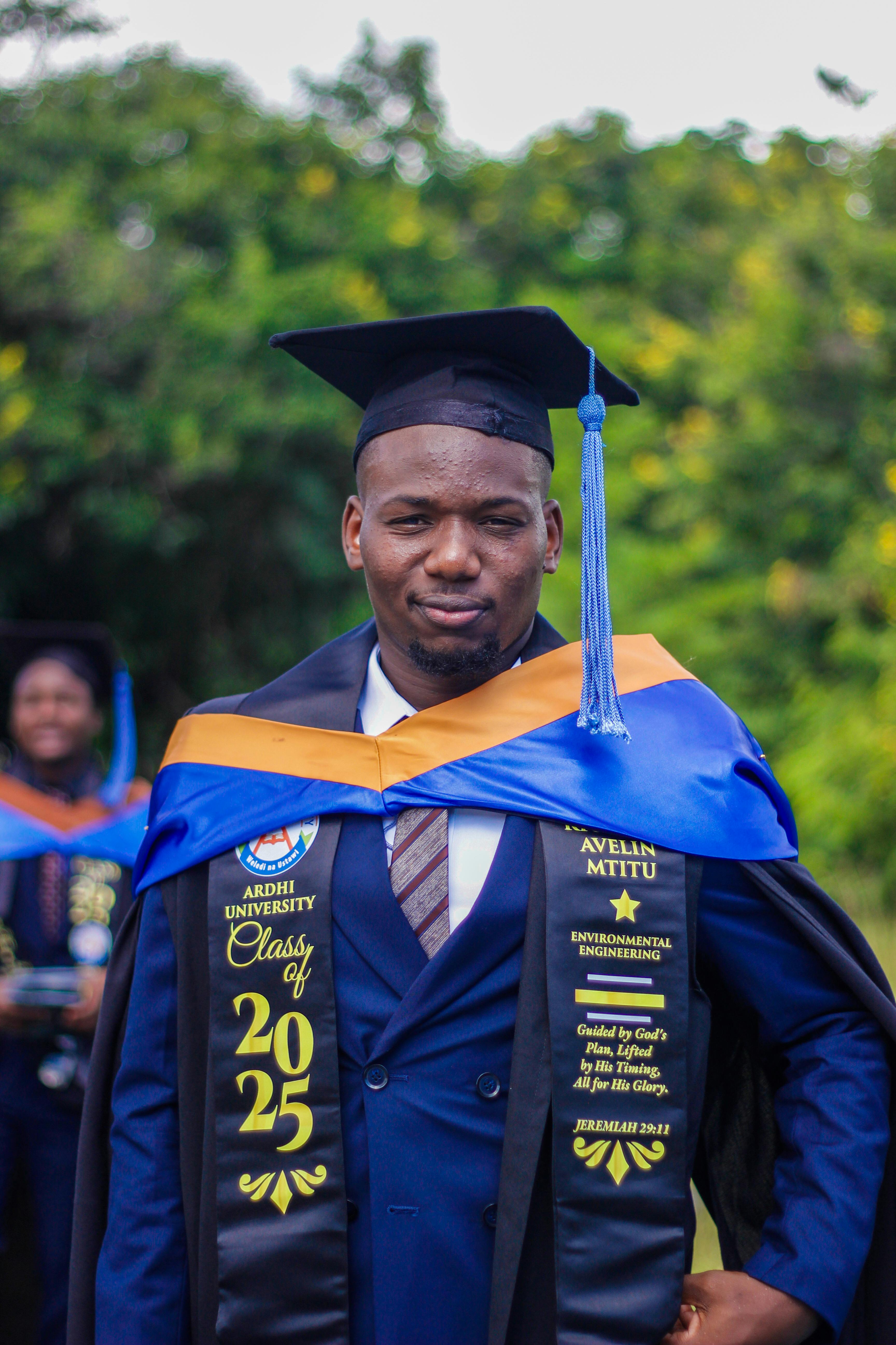 Proud 2025 graduate at Ardhi University during outdoor commencement.