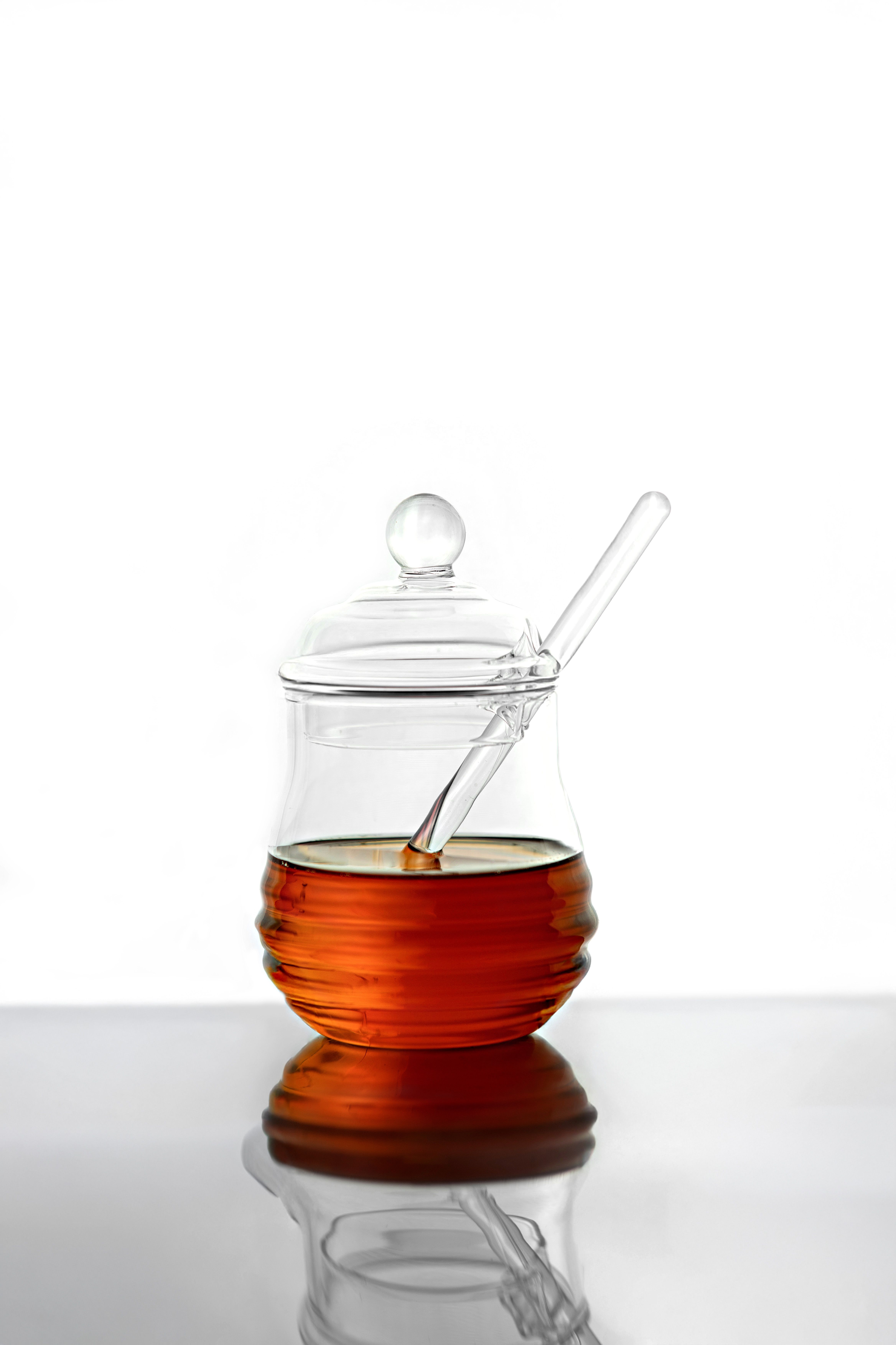 Elegant clear glass jar filled with honey, featuring a glass dipper, minimalist and sleek still life on a white background. - Factors to Consider When Selecting Honey