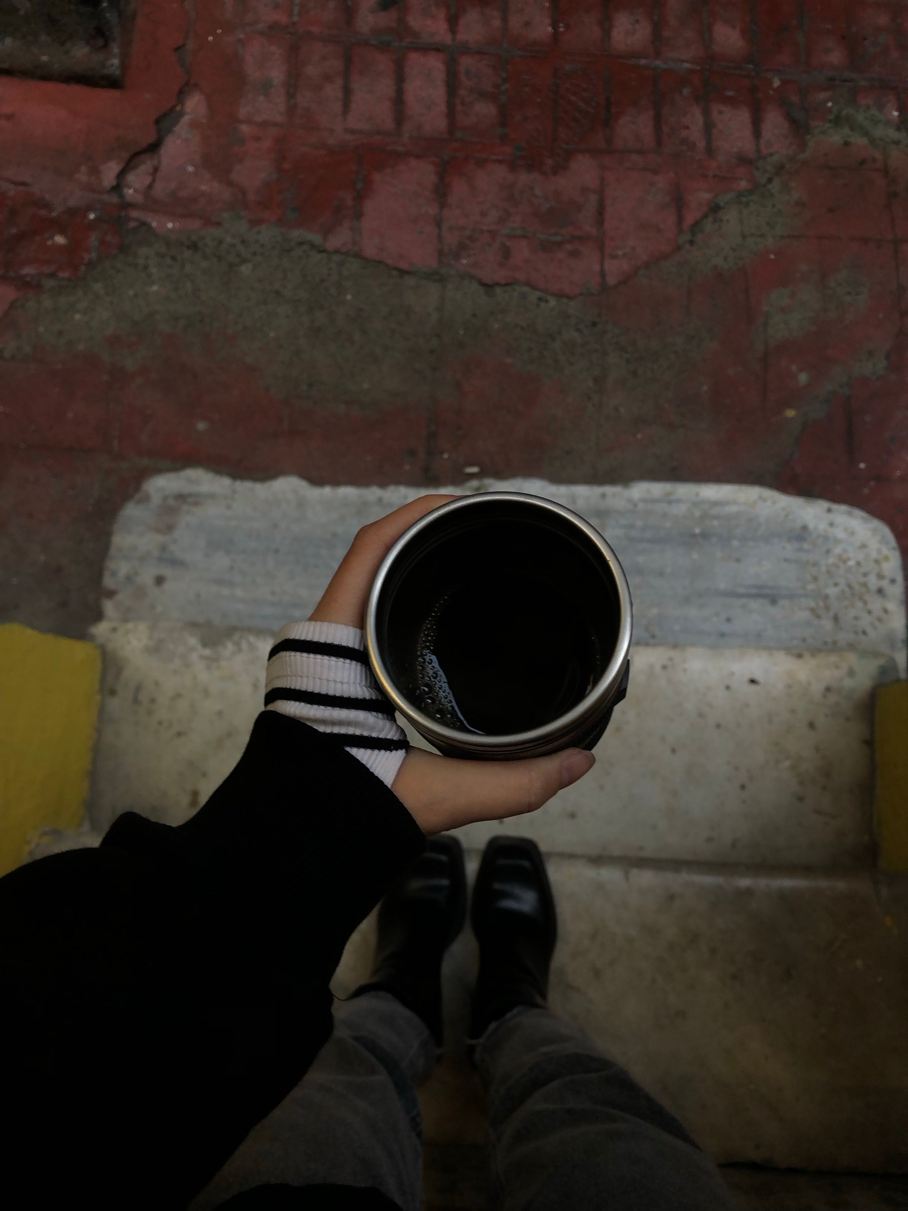 Close-up of a person holding a coffee cup, standing on outdoor steps.
