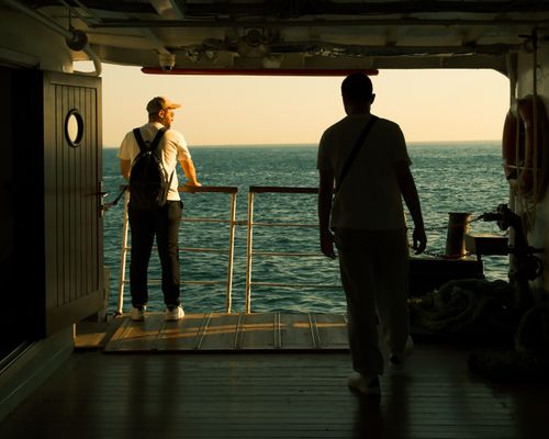 Free Two men standing on a ship deck, enjoying a sunset over the ocean. Stock Photo