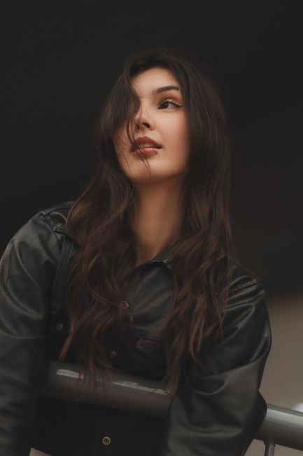 Confident woman in a black leather jacket gazing upward with a thoughtful expression outdoors.
