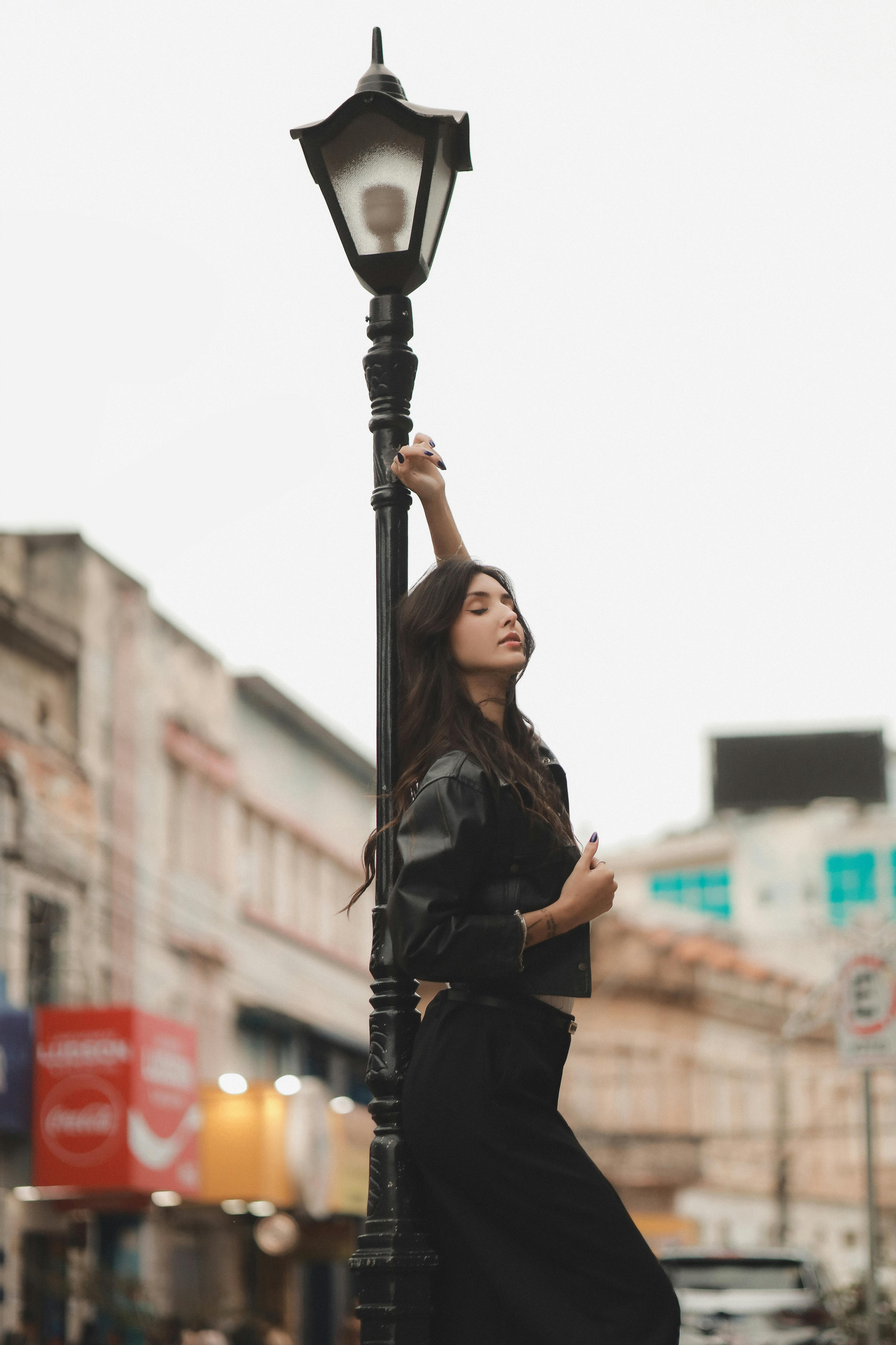 Fashionable woman in black outfit posing near a street lamp in an urban setting.