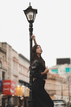 Fashionable woman in black outfit posing near a street lamp in an urban setting.