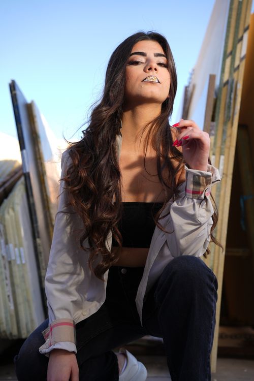 Free Confident young woman with long hair posing outdoors in an urban setting with a modern backdrop. Stock Photo