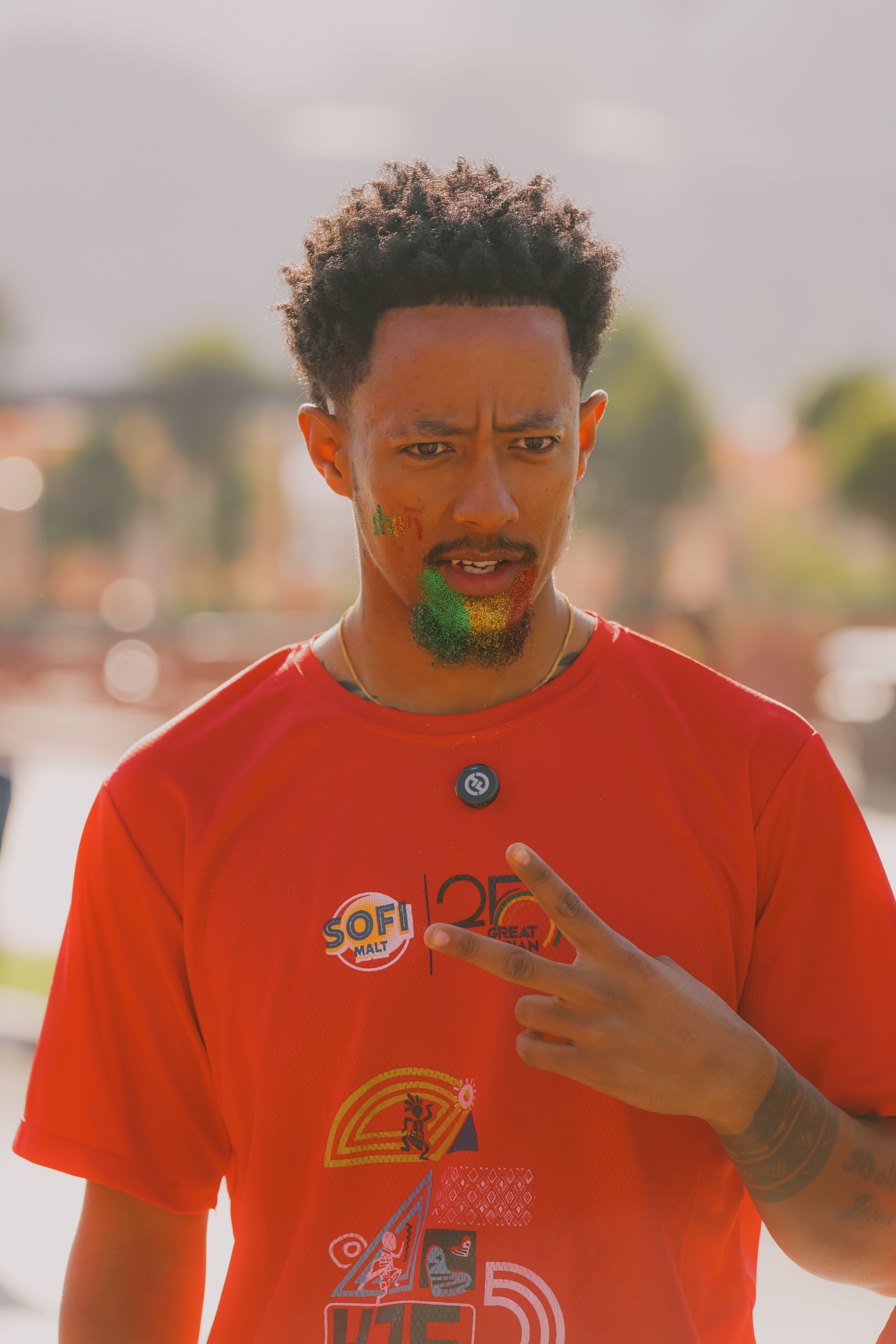 A young man in a red shirt with face paint celebrates outdoors during the day.