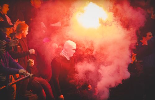 Free A dynamic scene of a crowd with a masked individual amidst vibrant smoke, creating a dramatic visual impact. Stock Photo
