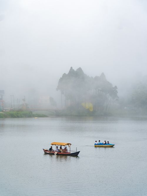 Free Boats glide across foggy Mirik Lake in West Bengal, offering a serene travel experience. Stock Photo