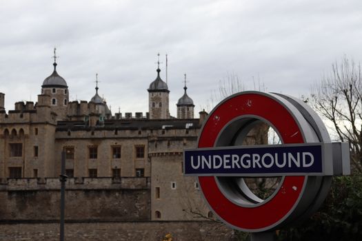 Iconic London Underground sign near the historical Tower of London on a cloudy day.