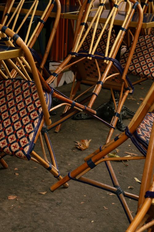 Free A stack of patterned wooden bistro chairs neatly arranged outside a cafe, suggesting a quiet moment. Stock Photo