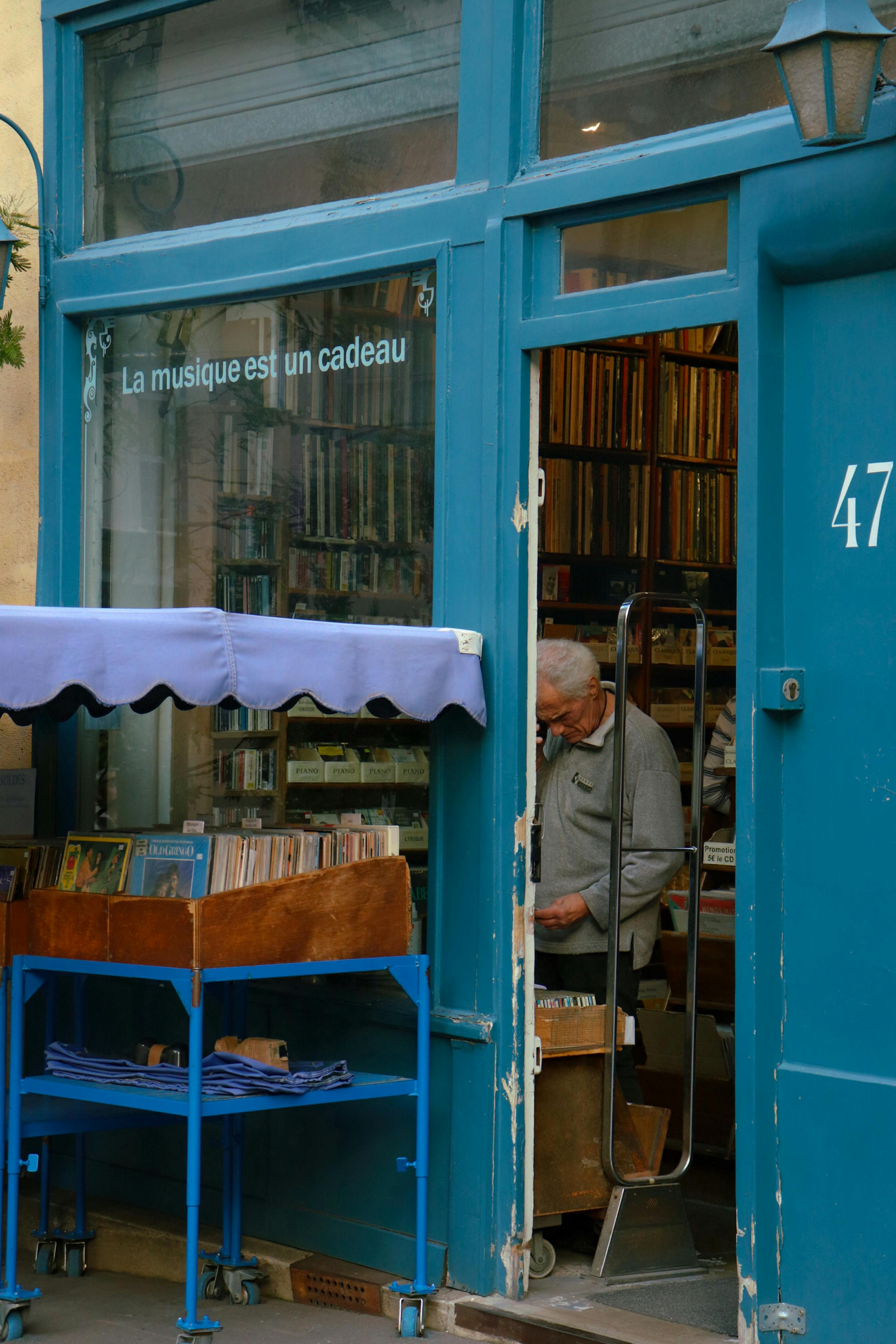 A quaint bookshop entrance with an elderly man browsing through books.