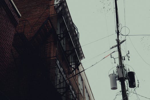 A moody urban scene with fire escapes and power lines on a rainy day.