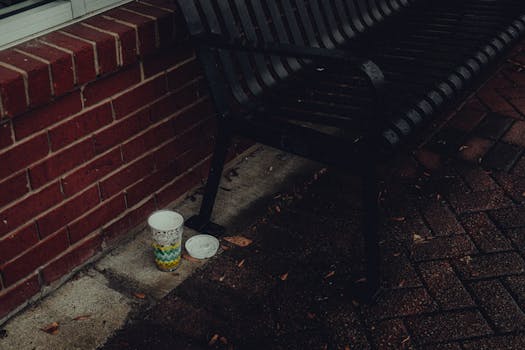 Dramatic urban scene with a lone coffee cup beside a bench on a rainy day.