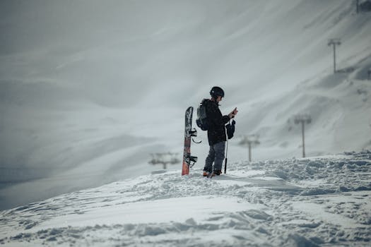 Snowboarder checks phone on snowy mountain during winter, ready to ride.