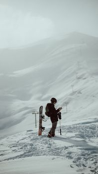 Snowboarder on a snowy mountain under a cloudy sky, preparing for a descent.