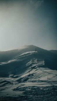Majestic snow-covered mountain with ski lift basking in twilight hues, showcasing winter tranquility.
