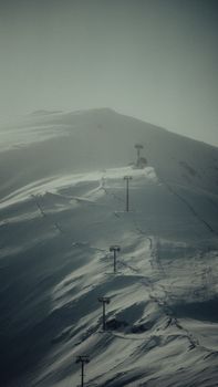 A snowy mountain landscape featuring a ski lift under an overcast sky, creating a serene winter scene.