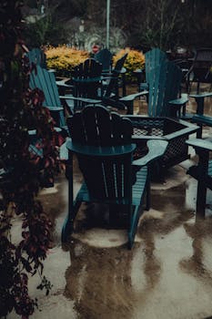 An atmospheric outdoor patio scene featuring rain-soaked chairs and reflective puddles, creating a moody ambiance.