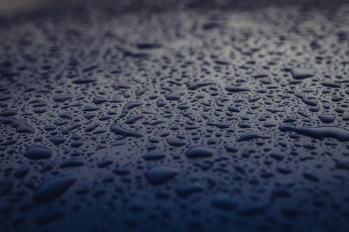 Free Macro photograph of water droplets glistening on a dark blue surface, creating a moody atmosphere. Stock Photo