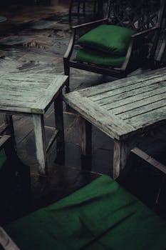 Weathered outdoor furniture with green cushions on wet, rain-soaked patio