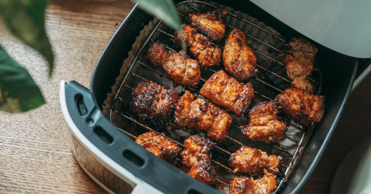 An air fryer basket pulled open with crispy chicken inside