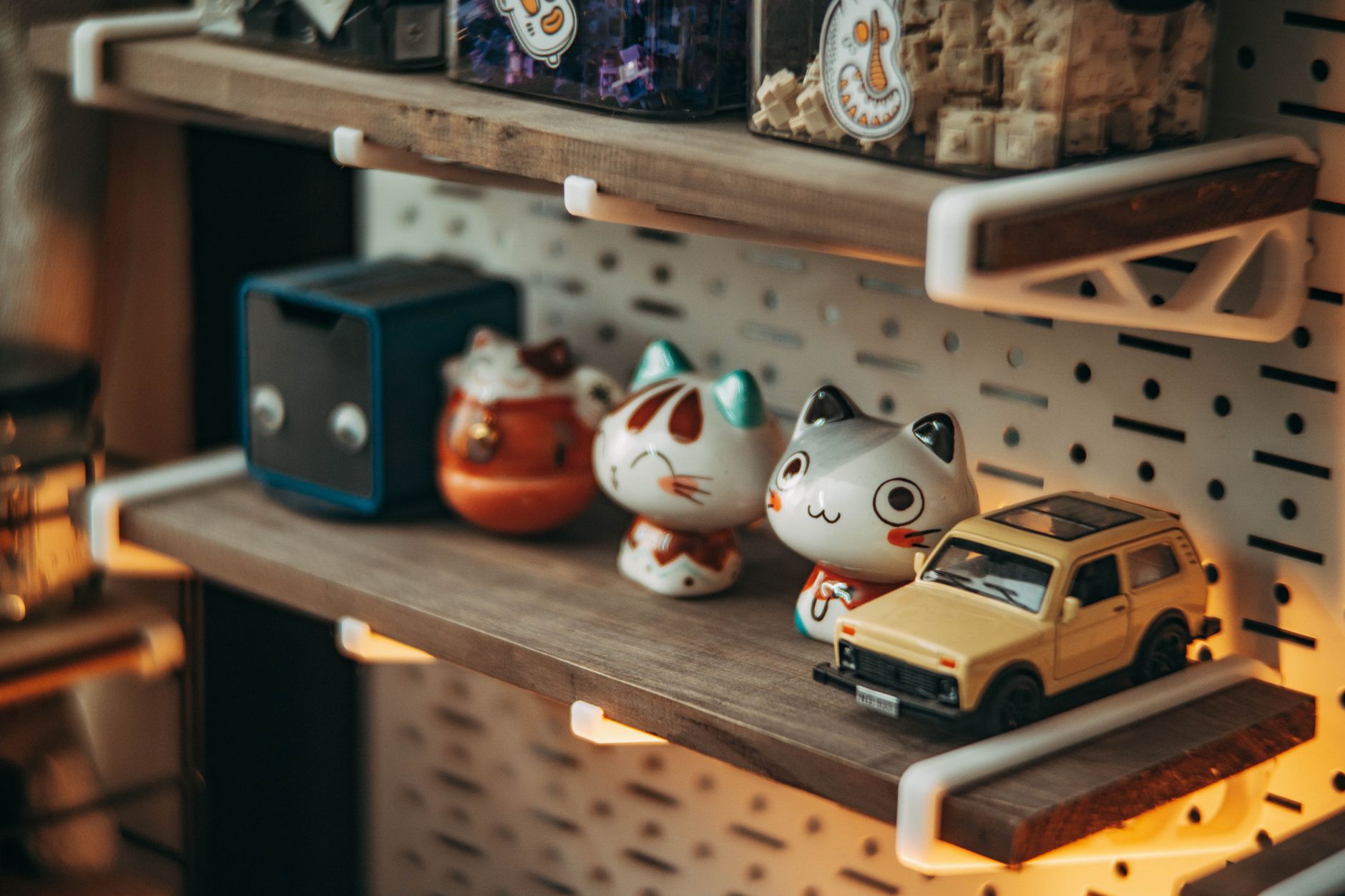 Wooden shelf with cute cat figurines and toy car, soft ambient lighting.