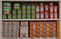 A vintage shelf displaying classic tins of Milo, Ovaltine, and teas in a retro shop setting.