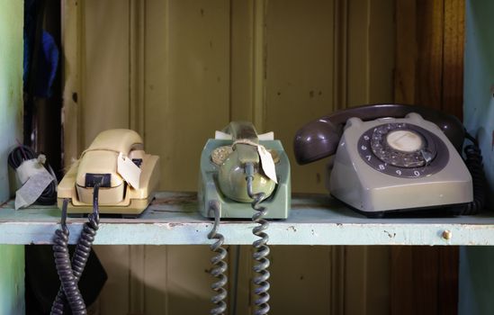 Collection of vintage rotary and push-button telephones on a shelf.