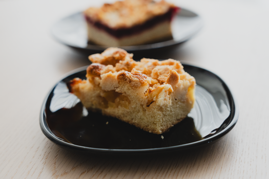 Close-up of a slice of apple streusel cake on a black plate, showcasing its crumbly topping.