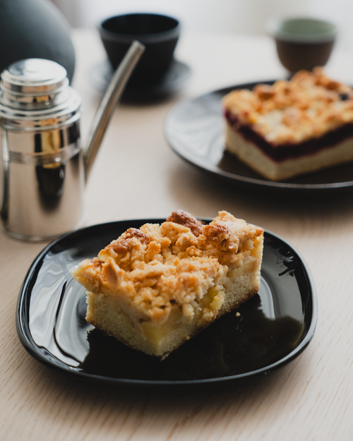 Free Close-up of a slice of streuselkuchen on a black plate with a coffee setup. Stock Photo