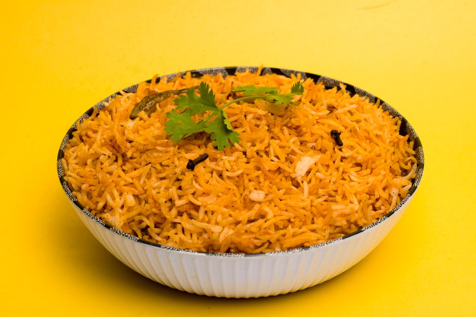 A bowl of golden turmeric-yellow rice with visible flecks of spice, served next to black beans and a wedge of lime.