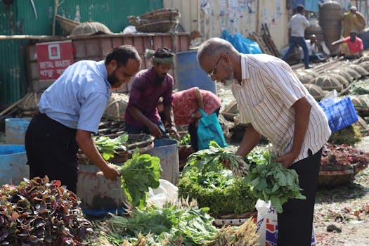 Lively outdoor street market featuring fresh greens and shoppers selecting produce in daylight.