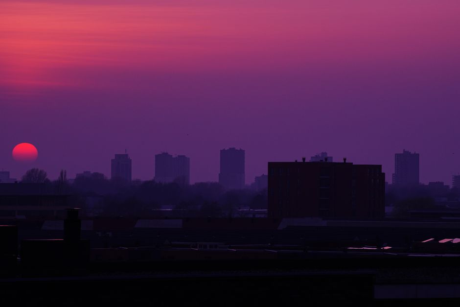 Silhouetted city skyline at sunset with a dramatic purple and orange sky.