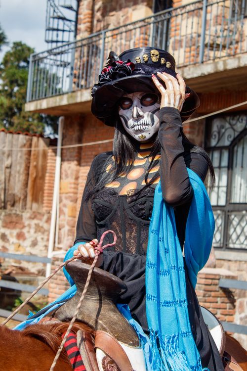 Free Woman in Day of the Dead makeup and costume, riding a horse with blue shawl in Mexico City. Stock Photo