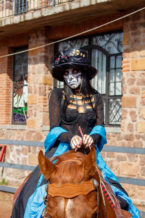 Free Woman with Day of the Dead makeup in vibrant costume riding a horse outdoors. Stock Photo