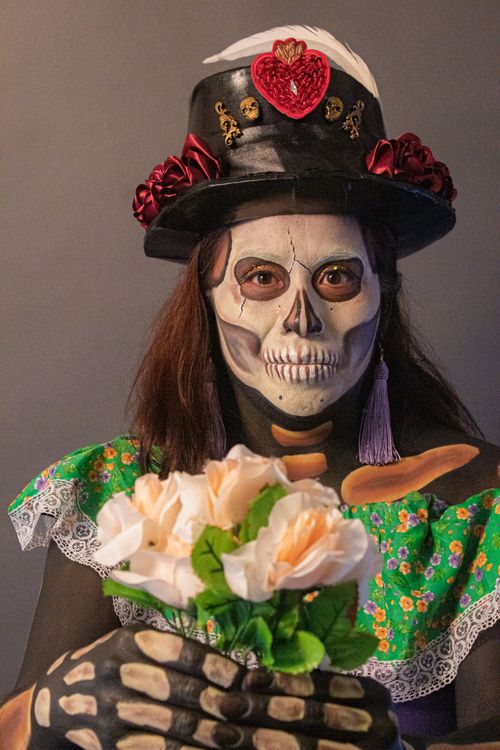 Free Woman in skeleton makeup and costume holding a bouquet, exemplifying Día de Muertos theme. Stock Photo