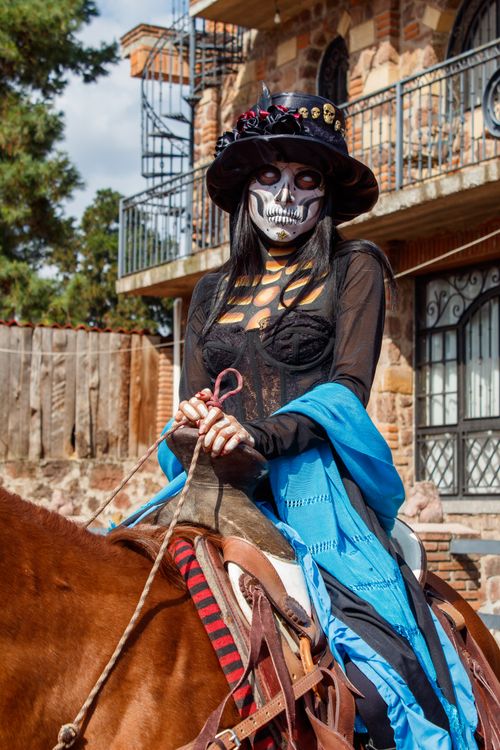 Free A person dressed in Day of the Dead attire rides a horse in Mexico City, showcasing traditional makeup and vibrant clothing. Stock Photo