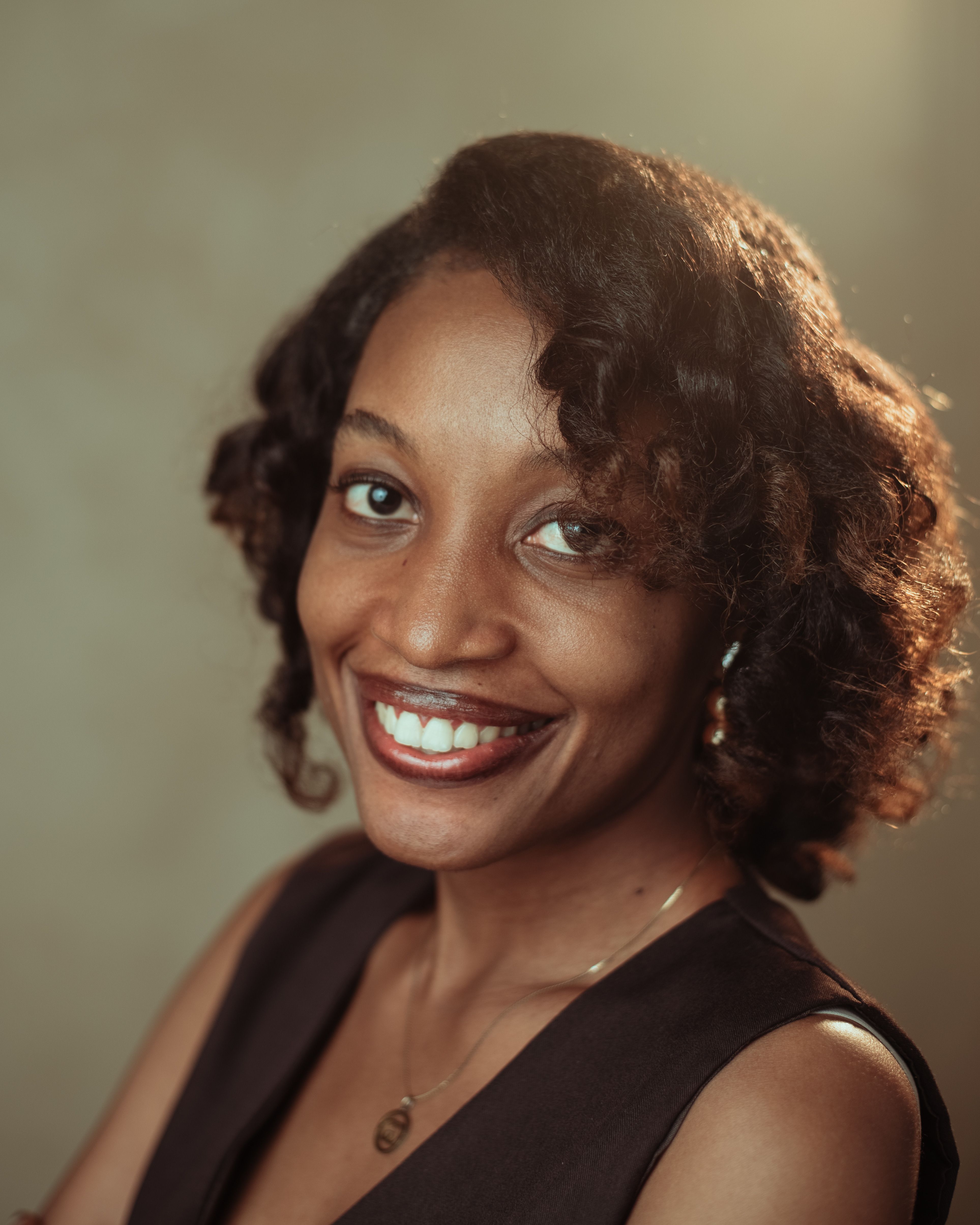 Smiling woman with curly hair captured in warm natural light, exuding warmth and charisma.