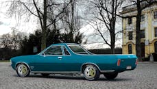 一辆经典的蓝色古董车停在鹅卵石街道上，靠近树木和一栋黄色建筑