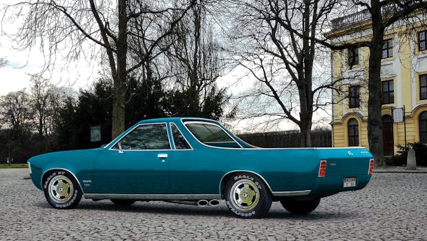 一辆经典的蓝色古董车停在鹅卵石街道上，靠近树木和一栋黄色建筑