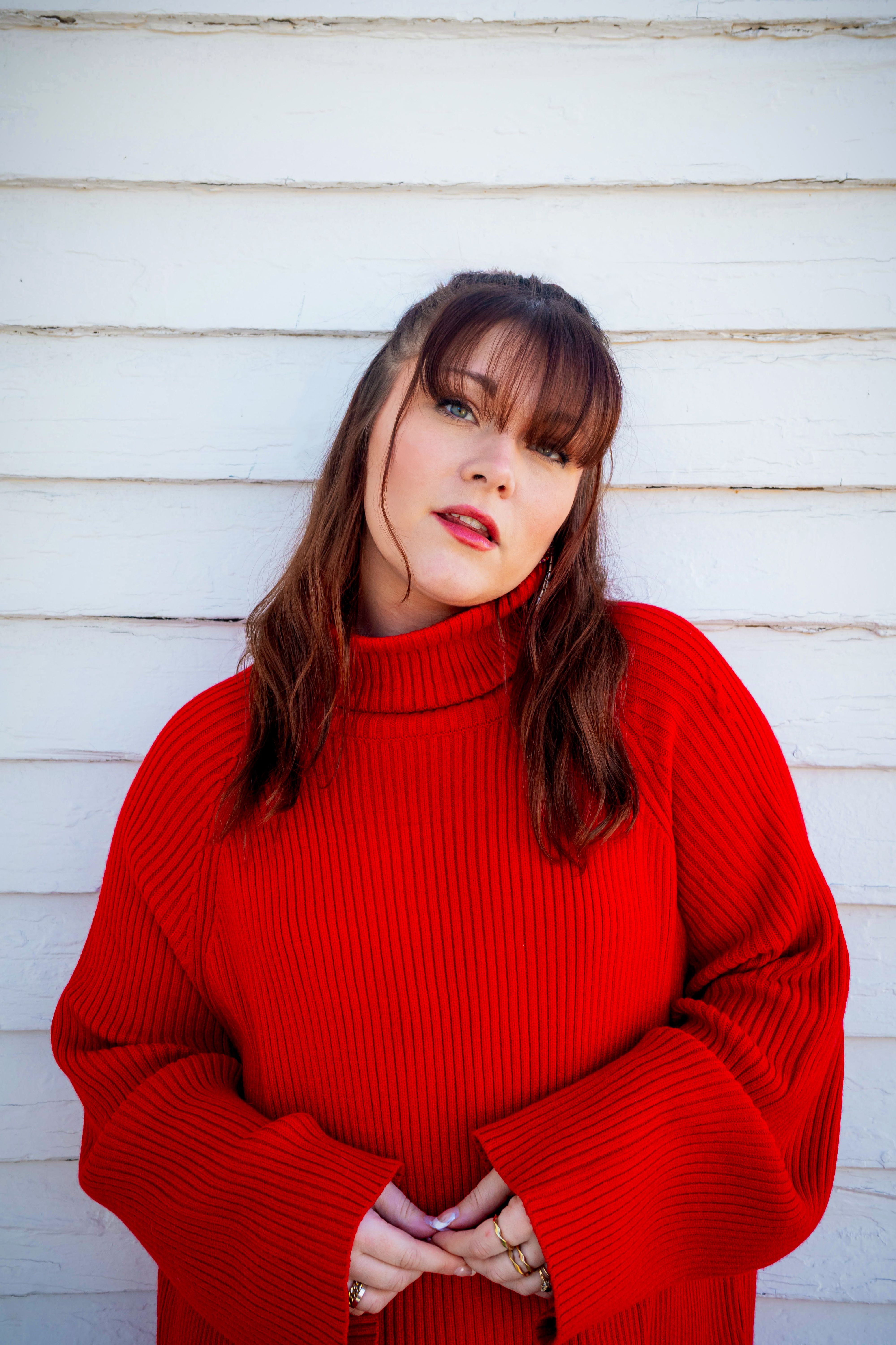 Stylish woman in red sweater posing against a wooden wall. Vibrant winter fashion.