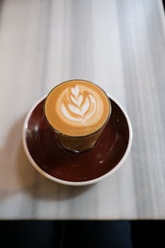 Artistic latte with heart leaf design in a glass cup on a marble table, perfect for coffee lovers.