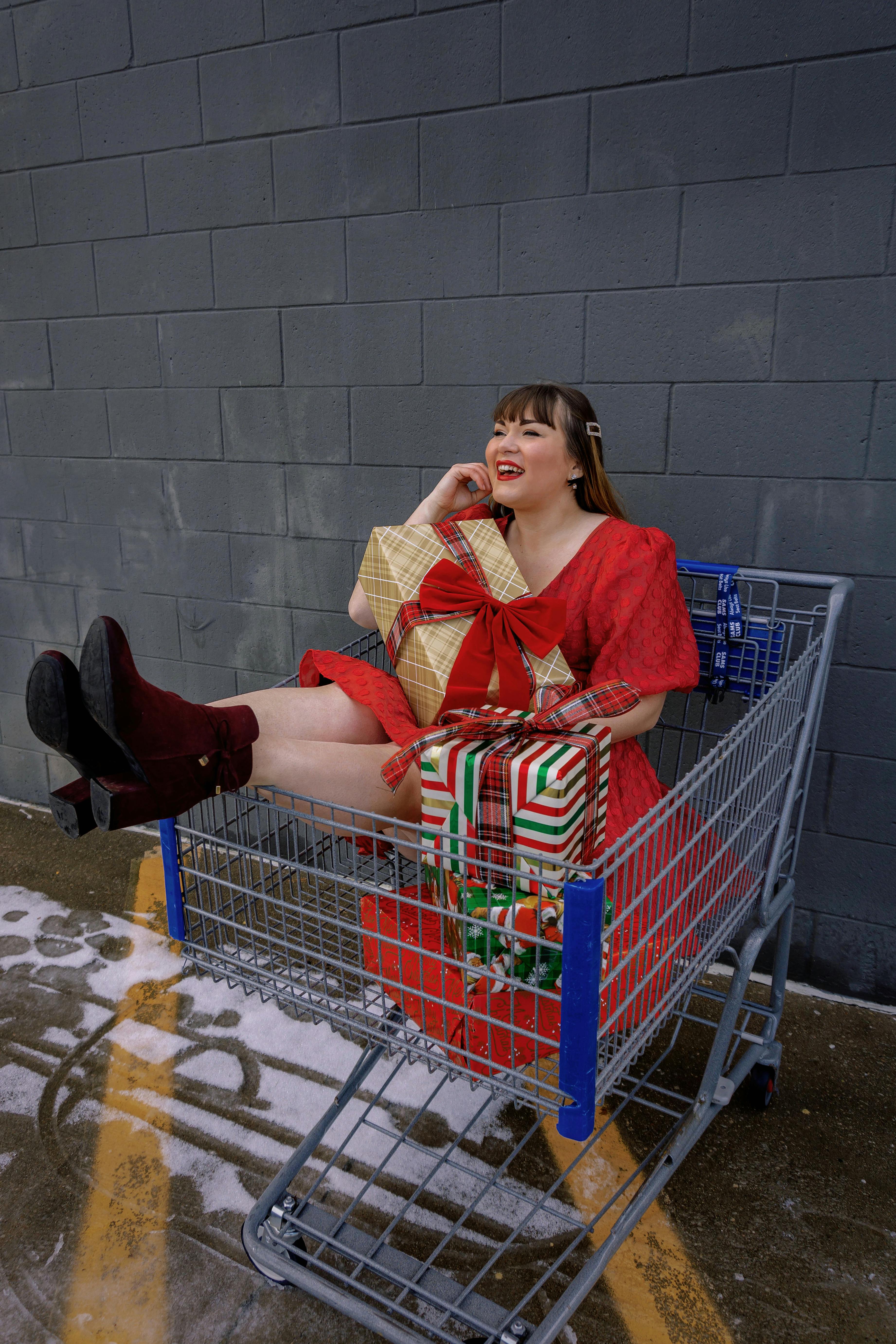 Woman in red dress with gifts in a shopping cart enjoying a festive moment.