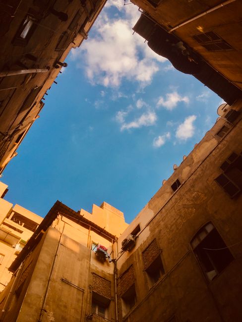 A serene view of a blue sky framed by rustic urban buildings in a courtyard.