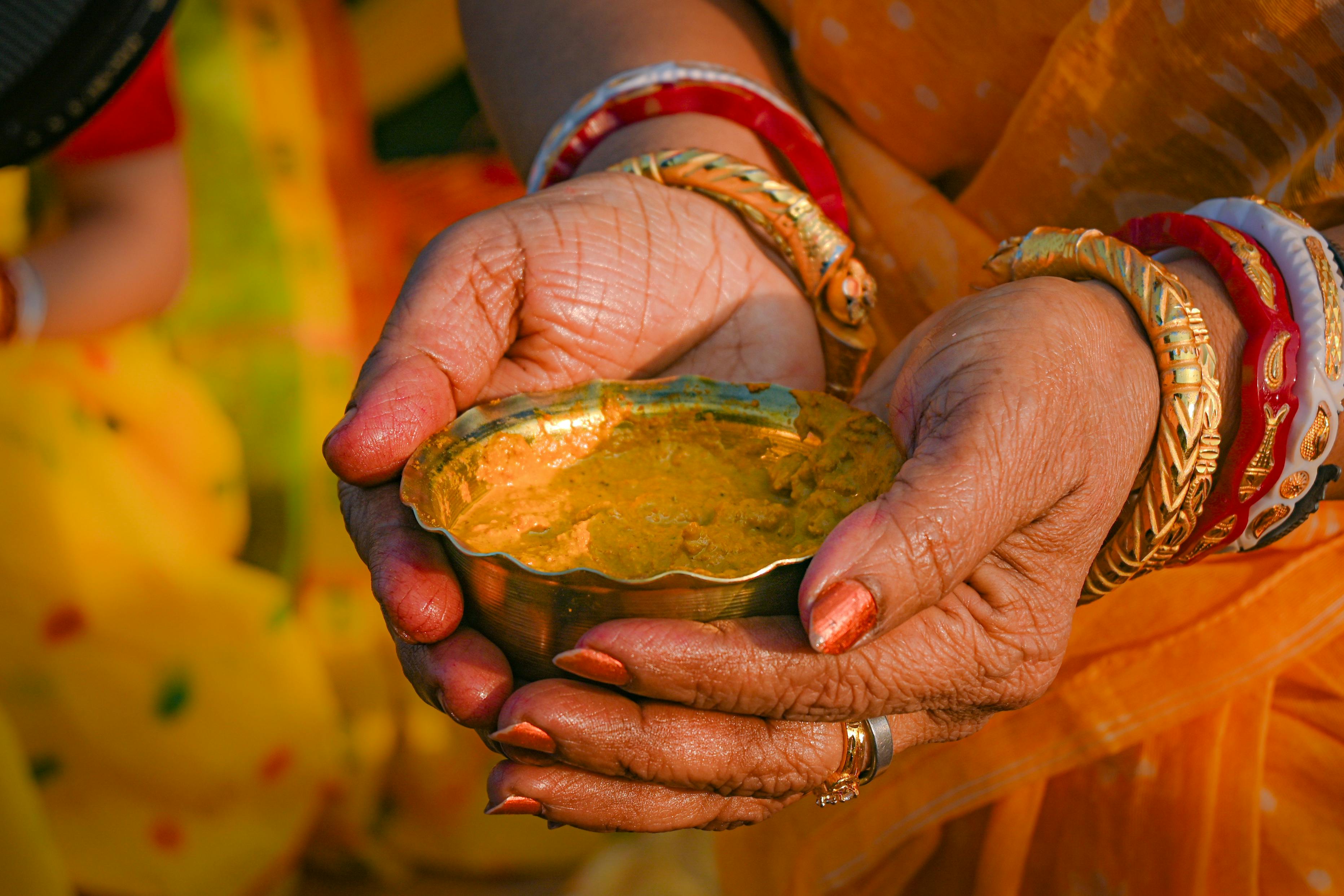Close-up of hands in traditional attire holding a bowl of turmeric paste, symbolizing Bengali rituals.