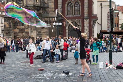 Free Street performer amazes crowd with giant rainbow soap bubbles in a bustling city square. Stock Photo