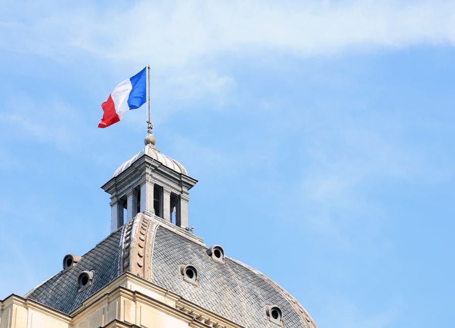 The French flag waves atop the dome of historic architecture in Paris, France.
