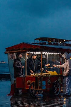Street food vendor serving customers in evening near waterfront. Captures night scene.