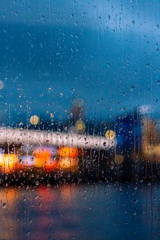 Blurred city lights seen through a raindrop-covered window, creating a tranquil evening mood.