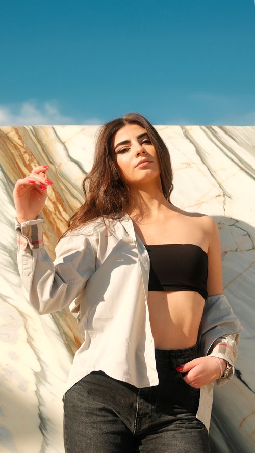 Free Confident young woman poses stylishly against a marble wall under a bright blue sky. Stock Photo